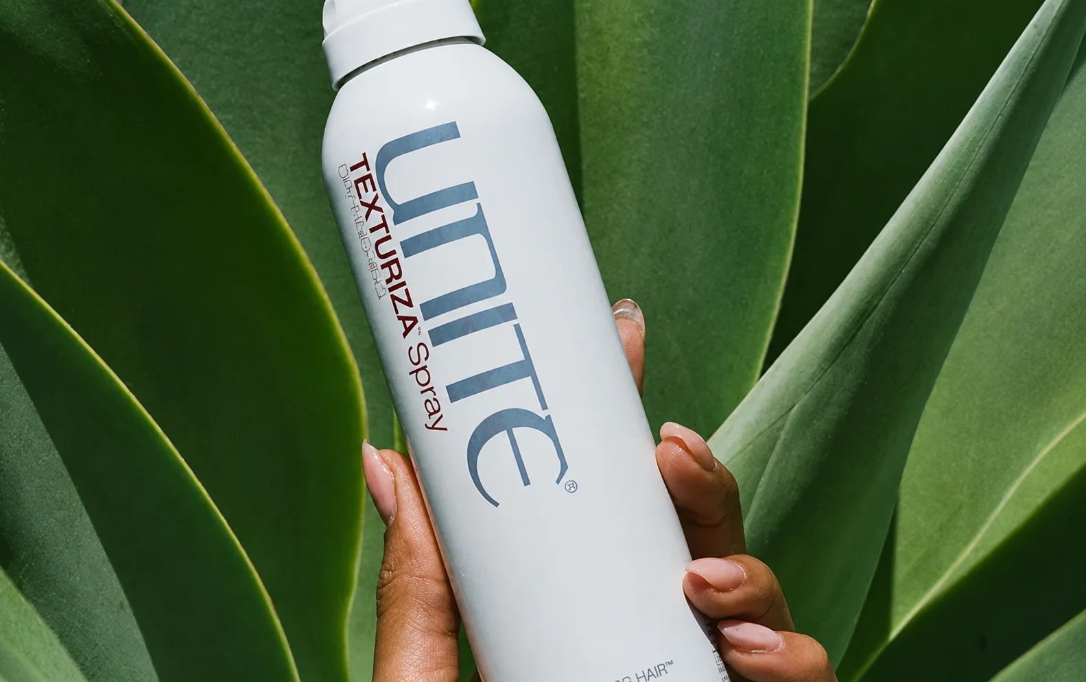 UNITE Hair haircare bottle held against a green leaf